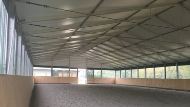 Interior view of an indoor riding arena with sand floor and open sides by equitent