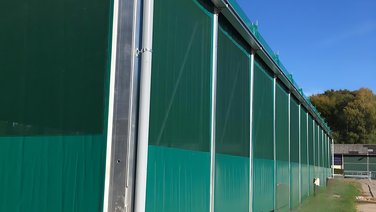 Side view of an indoor riding arena with green side tarpaulins