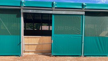 Exterior view of a sliding side door indoor riding arena from RÖDER with green PVC walls