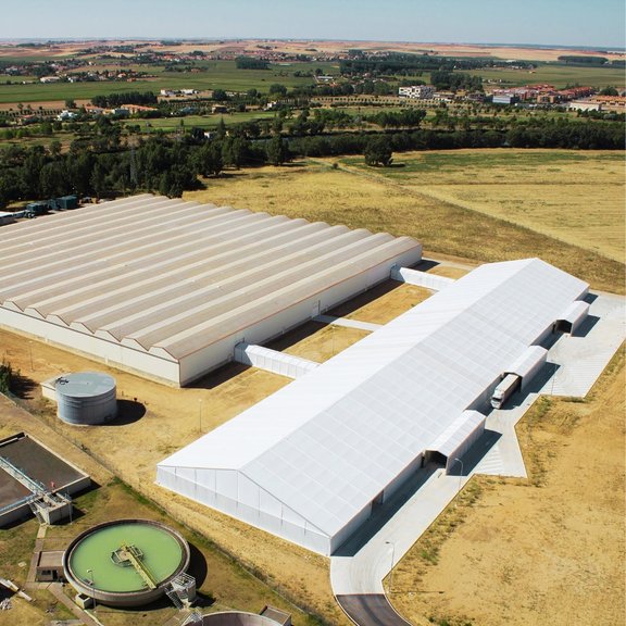 Vogelperspektive auf eine große Produktionshalle mit überdachten Wegen zu einer anderen Halle