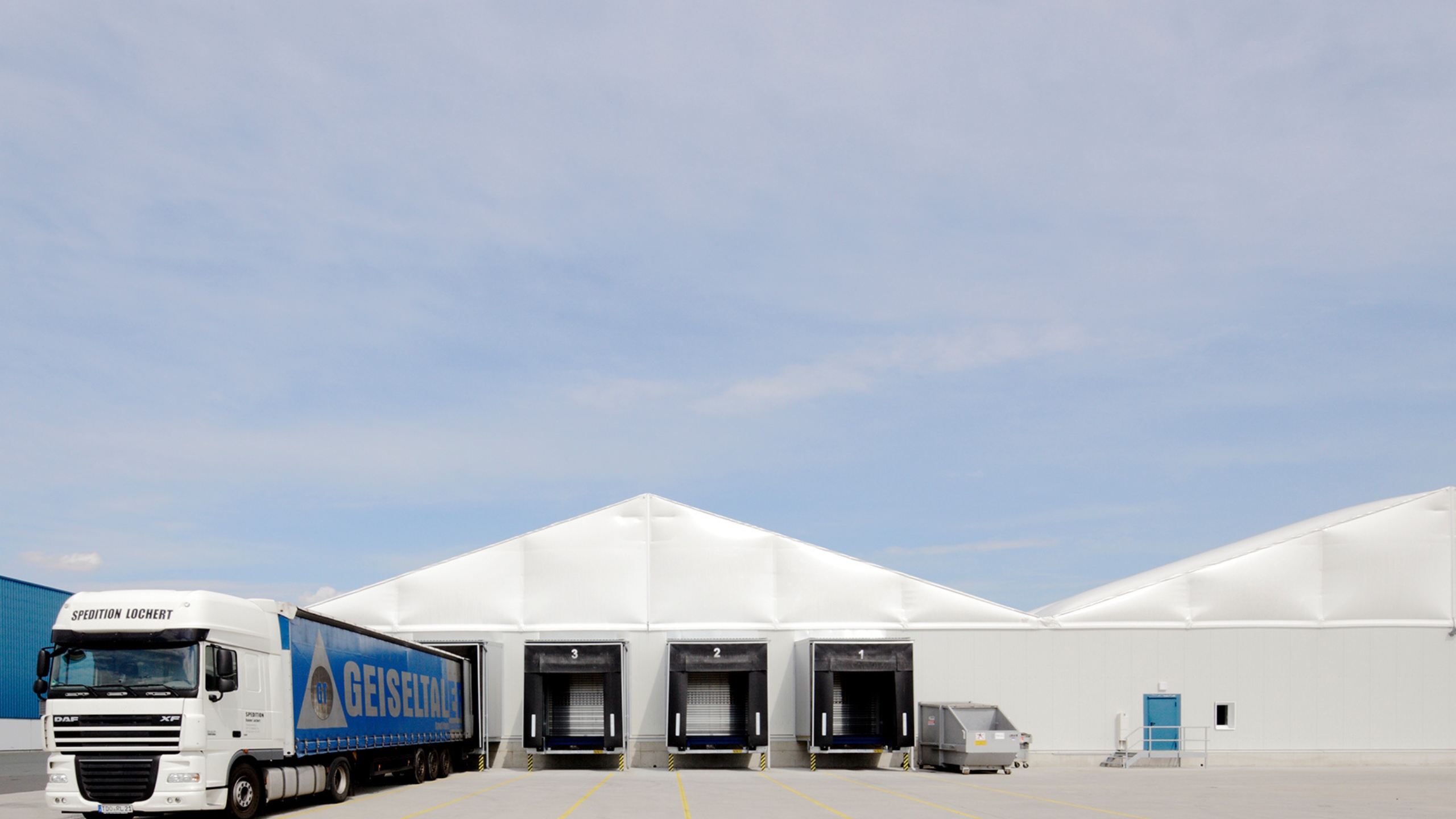 Front view of a multi-aisle lightweight hall with lorries and loading ramps Frontansicht_mit_Lkw_und_Stationen.jpg